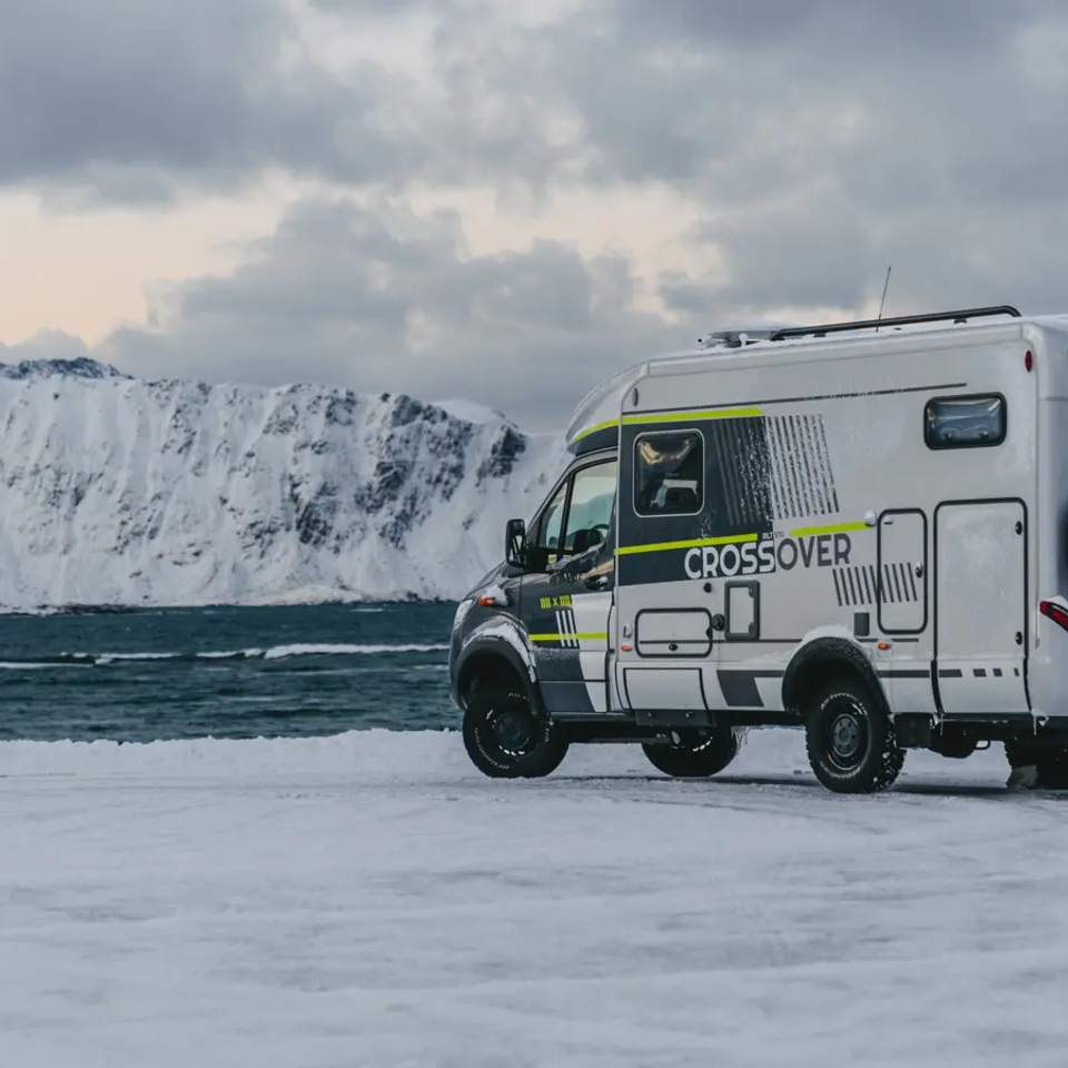 Sideudsigt af HYMER ML-T 570 CrossOver, højt sneklædt bjerg og havet i baggrunden