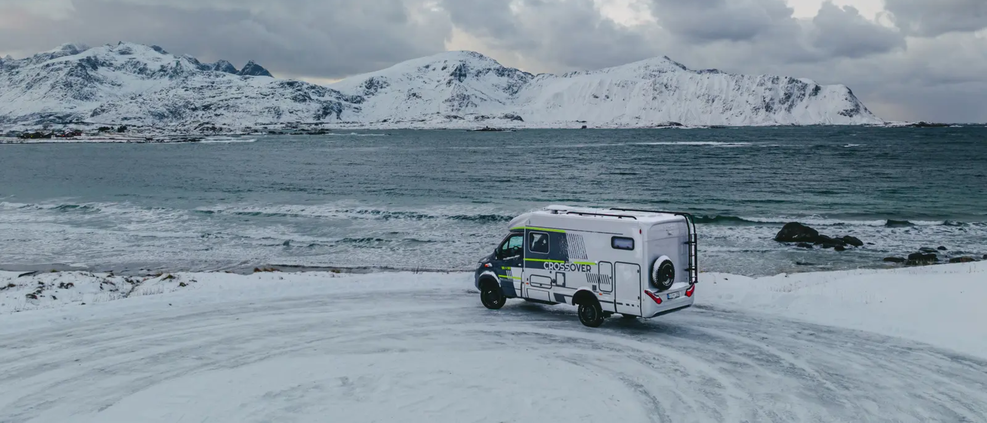 HYMER ML-T 570 CrossOver parkeret ved et udsigtspunkt, havet og sneklædte bjerge i baggrunden