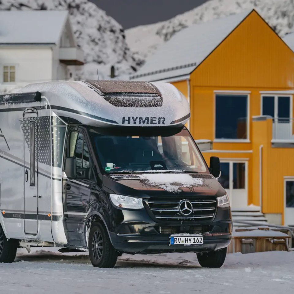 HYMER B-MC T BlackLine parkeret på en sneklædt sti, gule huse i baggrunden