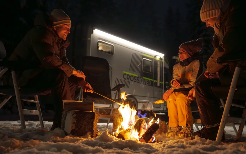 3 personer sidder ved et lejrbål og laver pindebrød, HYMER ML-T 570 CrossOver i baggrunden