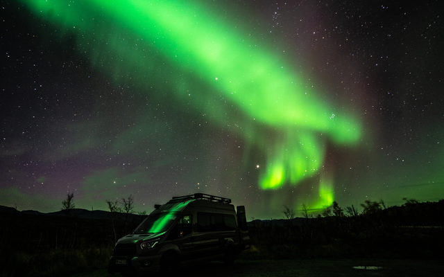 LMC Innovan Active avec ses portes arrière ouvertes, devant des aurores boréales vertes et un ciel étoilé violet