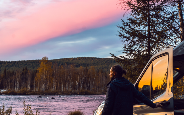Éric ouvrant la porte de l'LMC Innovan Active, regardant vers le lac/mer avec la forêt en arrière-plan et un ciel rose