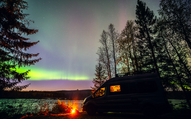 LMC Innovan Active devant un feu de camp, sous un ciel éclairé par des aurores boréales violettes et vertes