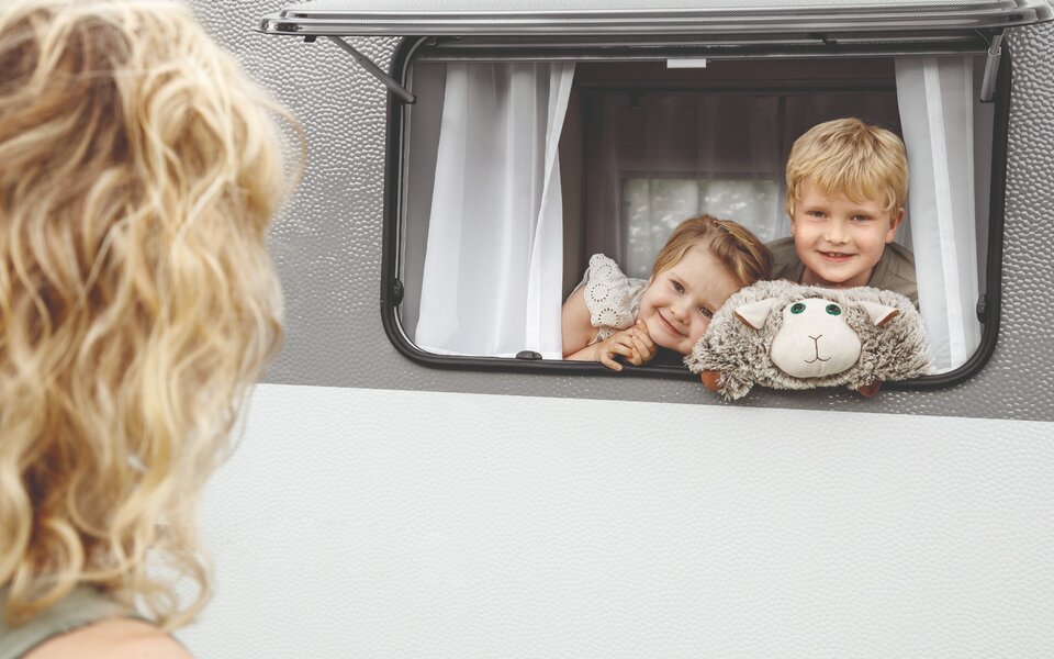 Das Bild zeigt zwei Kinder, welche aus dem LMC Sassino Wohnwagenfenster schauen.